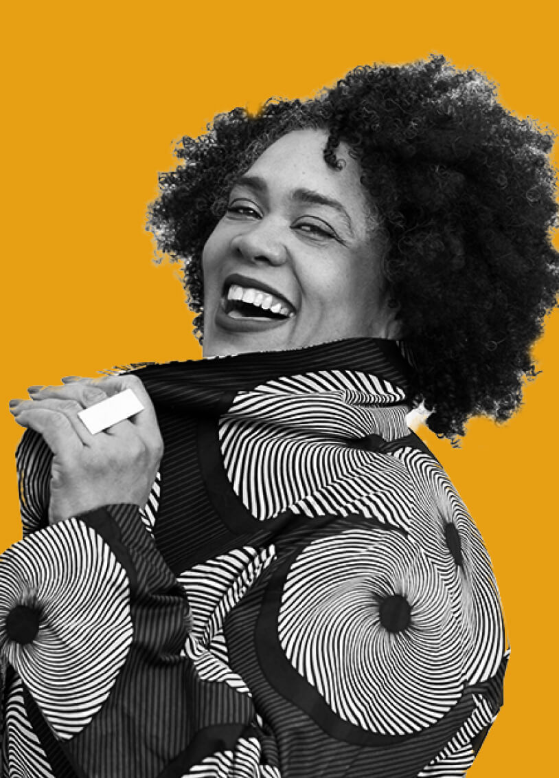 Woman with curly hair pulling the collar of her jacket, looking over her shoulder with a cheerful laughing smile. The image has a monochrome filter with an orange background.